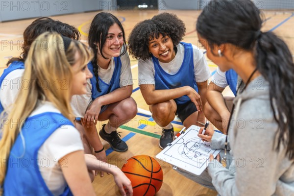 Female basketball coach drawing a play on a clipboard while explaining game strategy to her young multi ethnic female team players crouching in the court