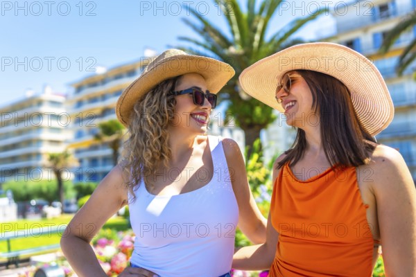 Two happy women wearing sunglasses and straw hats are enjoying their summer vacation in juan les pins, france