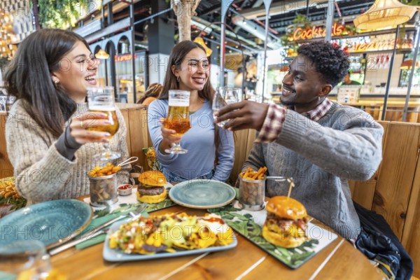 Happy multi ethnic friends toasting drinks and enjoying a delicious meal together at a lively restaurant, filled with laughter and joy
