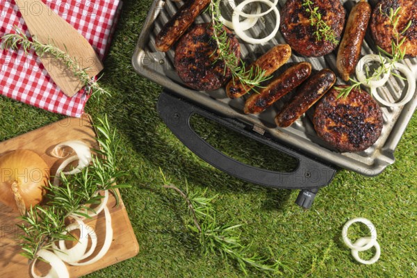Barbecue with sausages and burgers, decorated with rosemary and onions on a green lawn
