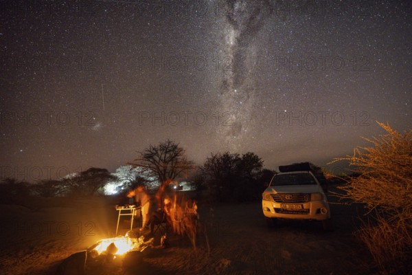 Tourists sitting around a campfire next to their off-road vehicle at night, night shot with starry sky and Milky Way, Kubu Island (Lekubu), Sowa Pan, Makgadikgadi Salt Pans, Botswana, Africa