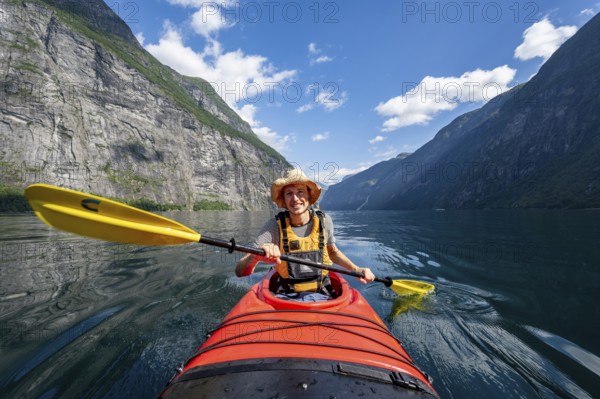 Kayak trip on the Geirangerfjord, young man paddling in red kayak, atmospheric fjord landscape, near Geiranger, Møre og Romsdal, Norway, Europe