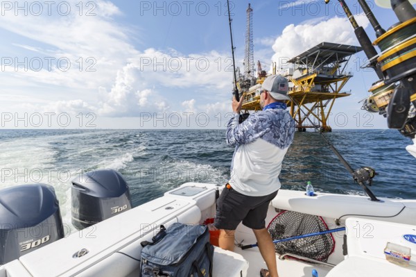 Fisherman trolling for fish near petroleum drilling rig in the Gulf of Mexico
