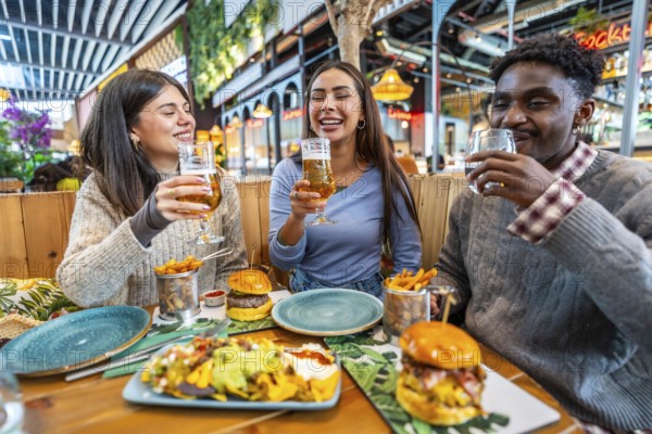 Happy multi ethnic friends are having fun together, eating burgers, nachos and fries, and drinking beer at restaurant
