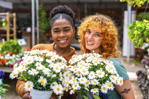 Two happy multi ethnic female garden center workers holding pots of white daisies smiling at the camera