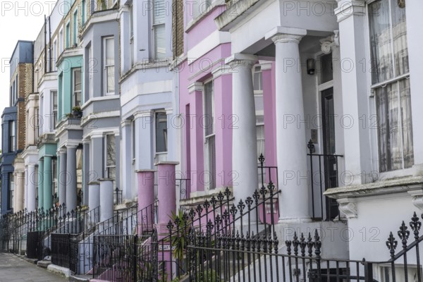 Pastel colored victorian terraced houses with ornate wrought iron fences create a picturesque street scene in london