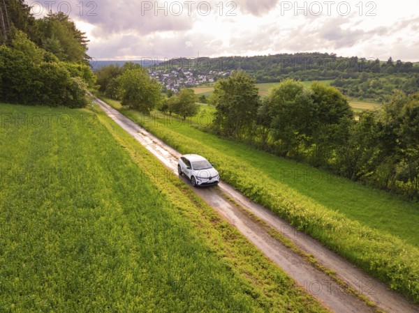 Car on narrow path between green meadows, view of village in the background, Deer E- CarSharing, Renault Megane electric car, Calw, Black Forest, Germany, Europe