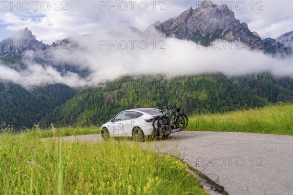 Car parked on a winding road in the impressive mountain landscape with fog and green meadows, electric car on holiday, Dolomites, South Tyrol, Dolomites, Italy, Europe