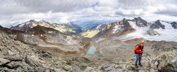 Mountain panorama, mountaineer with helmet on a rocky hiking trail, in high mountain landscape, view of blue glacier lakes, mountain peaks Königshofspitz and Hofmannspitze with glacier of the Übeltalferner, Stubai Alps, South Tyrol, Italy, Europe