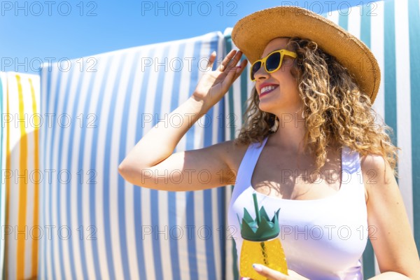 Young woman adjusting her straw hat while holding a tropical cocktail in a pineapple shaped glass at a beach resort
