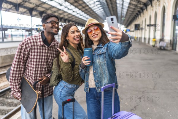 Three young tourists capturing a joyful selfie at a bustling train station, eagerly anticipating their next exciting adventure
