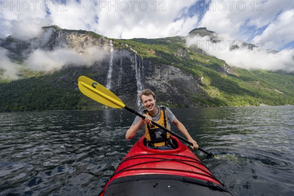 Kayak trip on the Geirangerfjord at the waterfall The Seven Sisters, Young man paddling in a kayak, atmospheric fjord landscape, near Geiranger, Møre og Romsdal, Norway, Europe