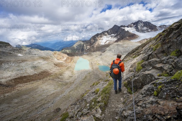 Mountaineer with helmet in high mountain landscape, view of blue glacial lakes, mountain peaks Königshofspitz and Hofmannspitze with glacier of the Übeltalferner, Stubai Alps, South Tyrol, Italy, Europe