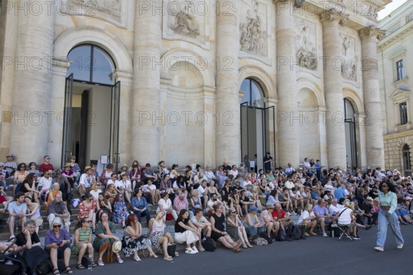 Visitors sit in the shade in front of St Hedwig's Cathedral without being able to see anything at the Staatsoper für alle, a free open-air concert with conductor Christian Thielemann and the Staatskapelle Berlin on Berlin's Bebelplatz, Berlin, 22 June 2025