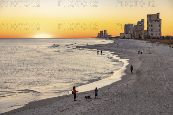 People walking and playing on the beach as the sun sets over the Gulf of Mexico at Gulf Shores, Alabama
