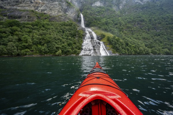 Kayak trip on the Geirangerfjord at the Freier waterfall, tip of a red kayak in the fjord, atmospheric fjord landscape, first person view, near Geiranger, Møre og Romsdal, Norway, Europe