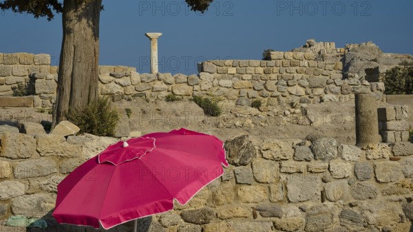 Ancient ruins with a red parasol in the foreground under a clear blue sky, Agios Stefanos Beach, Agios Stefanos Basilica, Chapel of Agios Nikolaos, Kastri Island, Kos, Dodecanese, Greek Islands, Greece, Europe