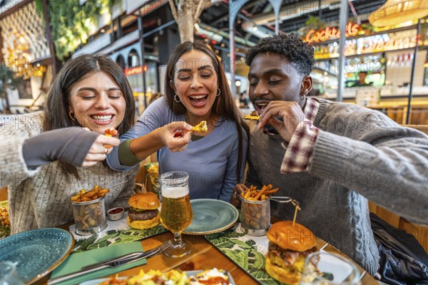Three cheerful multi ethnic friends sharing nachos and burgers, enjoying a meal together at a restaurant