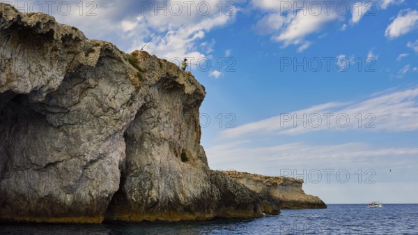 Person fishing from a rocky cliff under a cloudy sky, boat trip around the island of Ortigia, Isola di Ortigia, Syracuse, Sicily, Italy, Europe