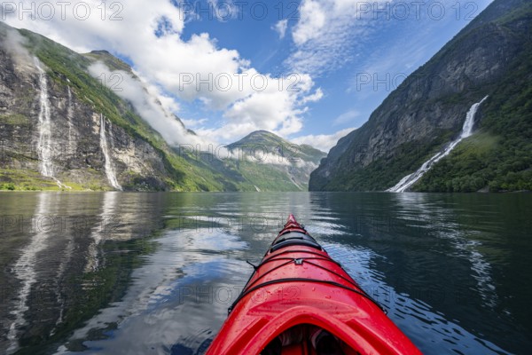 Kayak trip on the Geirangerfjord with waterfall The Seven Sisters and Freier Waterfall, tip of a red kayak in the fjord, atmospheric fjord landscape with reflection, first person view, near Geiranger, Møre og Romsdal, Norway, Europe