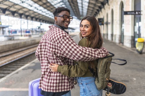 Young multi ethnic couple of tourists hugging at the train station, ready to start their vacation