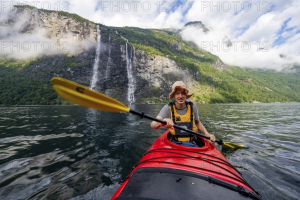 Kayak trip on the Geirangerfjord at the waterfall The Seven Sisters, Young man paddling in a kayak, atmospheric fjord landscape, near Geiranger, Møre og Romsdal, Norway, Europe