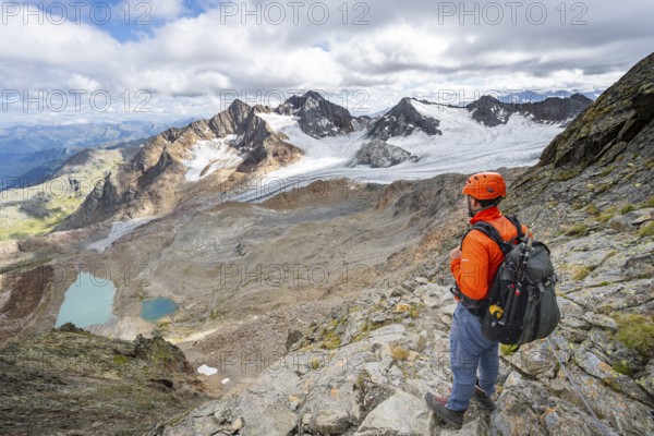 Mountaineer with helmet in high mountain landscape, view of blue glacier lakes, mountain peaks Königshofspitz and Hofmannspitze with glacier of the Übeltalferner, Stubai Alps, South Tyrol, Italy, Europe