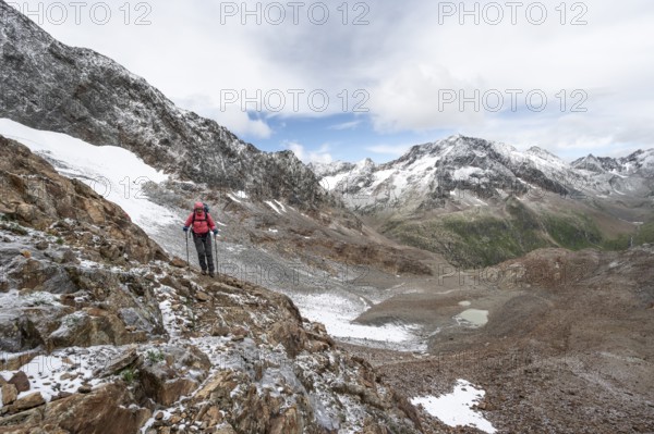Mountaineer on a rocky hiking trail in a steep rocky mountain landscape with fresh snow in summer, mountain peak Roter Knopf in the background, descent from the Hornscharte on the Wiener Höhenweg, Schobergruppe, Hohe Tauern National Park, Carinthia, Austria, Europe