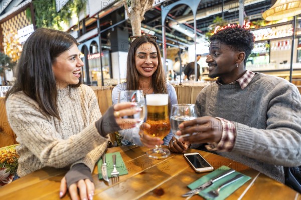 Multi ethnic friends smiling and toasting with beer and water at a brewery pub, enjoying their time together