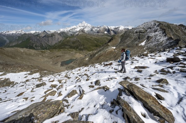 Mountaineer in boulder terrain with fresh snow in summer, ascent to the summit Böses Weibl, view of the mountain landscape with Kesselkeessee, snow-covered summit of the Großglockner in the background, Wiener Höhenweg, Schober group, Hohe Tauern National Park, Carinthia, Austria, Europe