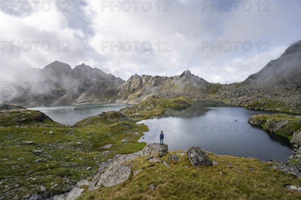 Mountaineer on a rock in front of mountain lakes Wangenitzsee and Kreuzsee, cloudy mountain peaks in the morning, Schober group, Hohe Tauern National Park, Carinthia, Austria, Europe