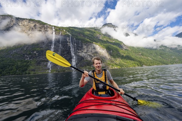 Kayak trip on the Geirangerfjord at the waterfall The Seven Sisters, Young man paddling in a kayak, atmospheric fjord landscape, near Geiranger, Møre og Romsdal, Norway, Europe