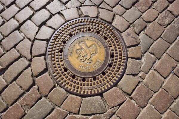 Manhole cover, 350 years of the Peace of Westphalia, 1648 to 1998, golden, cobblestones, biblical symbol, dove of peace, Münster, Münsterland, independent city, North Rhine-Westphalia, Germany, Europe