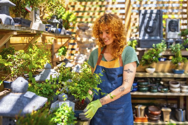 Female gardener wearing gloves, carefully holding a small bonsai tree while tending to plants in a vibrant nursery filled with greenery