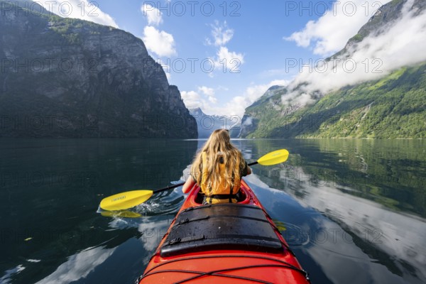 Kayak trip on the Geirangerfjord, young woman paddling in a red kayak, atmospheric fjord landscape, Møre og Romsdal, Norway, Europe