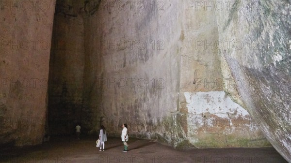 Cave Ear of Dionysus, Large rock cave with several people exploring the dark surroundings, Neapolis Archaeological Park, Syracuse, Sicily, Italy, Europe