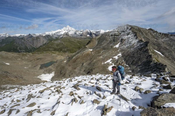 Mountaineer in boulder terrain with fresh snow in summer, ascent to the summit Böses Weibl, view of the mountain landscape with Kesselkeessee, snow-covered summit of the Großglockner in the background, Wiener Höhenweg, Schober group, Hohe Tauern National Park, Carinthia, Austria, Europe
