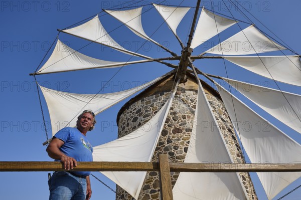 A man stands in front of a windmill with white sails under a clear blue sky, Windmill, Antimacheia, Kos, Dodecanese, Greek Islands, Greece, Europe