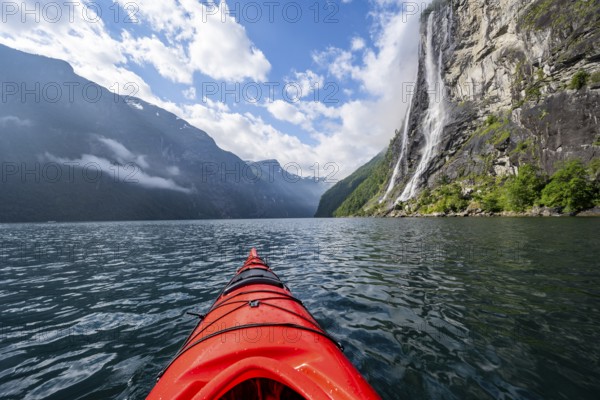 Kayak trip on the Geirangerfjord at the waterfall The Seven Sisters, tip of a red kayak in the fjord, atmospheric fjord landscape, first person view, near Geiranger, Møre og Romsdal, Norway, Europe