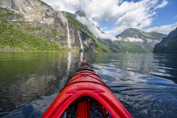 Kayak trip on the Geirangerfjord with waterfall The Seven Sisters, tip of a red kayak in the fjord, atmospheric fjord landscape with reflection, first person view, near Geiranger, Møre og Romsdal, Norway, Europe