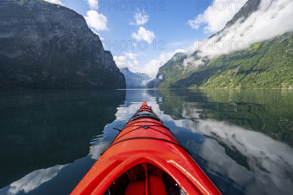 Kayak trip on the Geirangerfjord, tip of a red kayak in the fjord with reflection, atmospheric fjord landscape, first person view at Geiranger, Møre og Romsdal, Norway, Europe