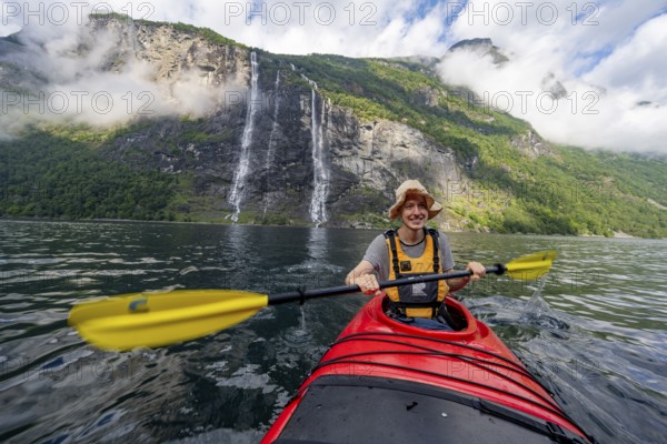 Kayak trip on the Geirangerfjord at the waterfall The Seven Sisters, Young man paddling in a kayak, atmospheric fjord landscape, near Geiranger, Møre og Romsdal, Norway, Europe