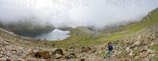 Mountaineer on a hiking trail, cloudy mountain landscape with mountain lake, Middle Moarer Egetsee, Seven Lakes Hike, Stubai Alps, near Ridnaun, South Tyrol, Italy, Europe