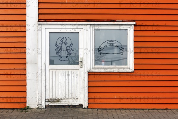 Colourful lobster shack, orange wooden façade with door and window, lobster pictogram, façade detail in the harbour, Heligoland, Schleswig-Holstein, Germany, Europe