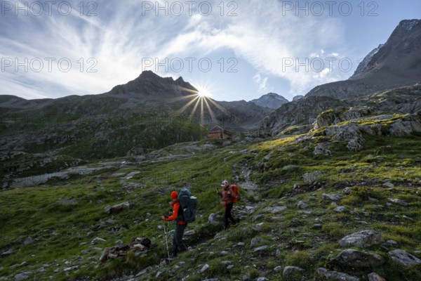 Mountaineers on a hiking trail, mountain hut Elberfelderhütte in front of a rocky mountain landscape, sun star in the morning, in the upper Gössnitz valley, Wiener Höhenweg, Schober group, Hohe Tauern National Park, Carinthia, Austria, Europe