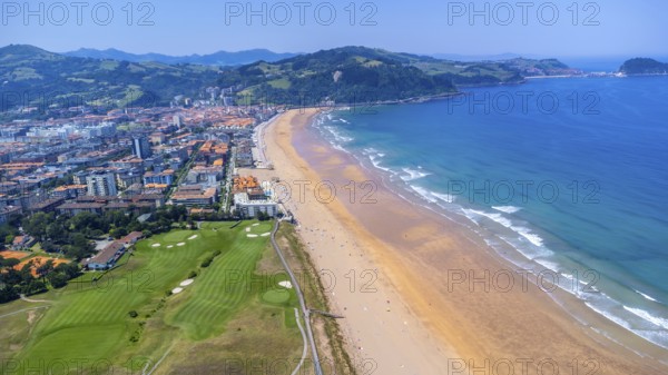 Aerial view of zarautz, gipuzkoa, showcasing the golden sands, turquoise waters, and green hills of the basque country during a sunny summer day, Spain.