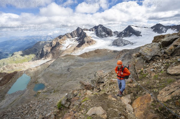 Mountaineer with helmet in high mountain landscape, view of blue glacier lakes, mountain peaks Königshofspitz and Hofmannspitze with glacier of the Übeltalferner, Stubai Alps, South Tyrol, Italy, Europe