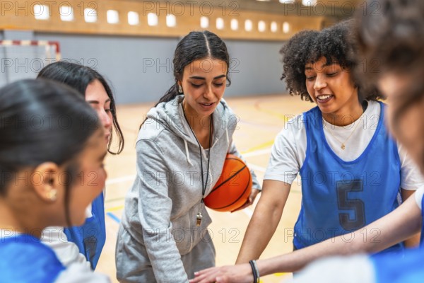 Female basketball coach motivating and inspiring her team during a time out, holding the ball and putting their hands together