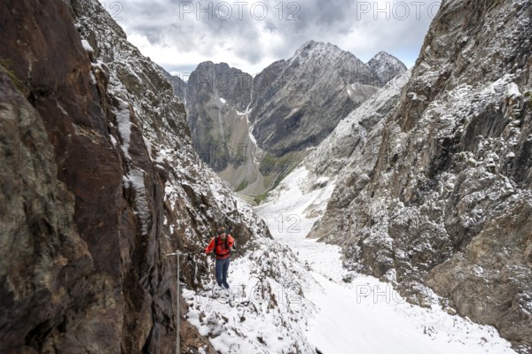 Mountaineer on a rope-secured path in a steep rocky mountain landscape with fresh snow in summer, behind mountain peaks Großer Friedrichskopf and Georgskopf, ascent to Hornscharte, Schobergruppe, Hohe Tauern National Park, Carinthia, Austria, Europe