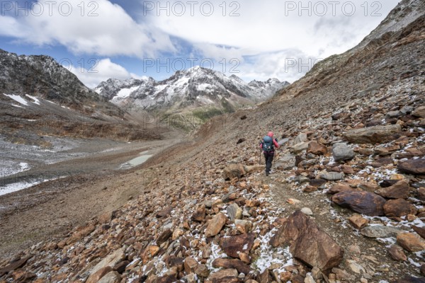 Mountaineer on hiking trail in steep rocky mountain landscape with fresh snow in summer, mountain peak Roter Knopf in the background, descent from the Hornscharte on the Wiener Höhenweg, Schober group, Hohe Tauern National Park, Carinthia, Austria, Europe
